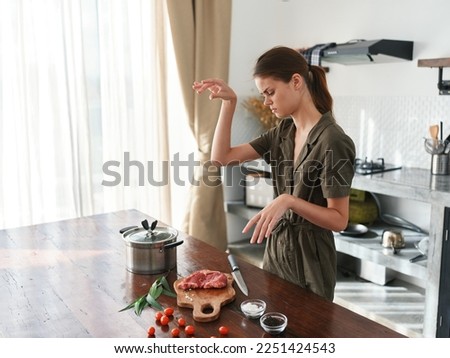 A woman in the kitchen prepares dinner from meat and vegetables and spices on a wooden table against the backdrop of a stylish kitchen, fresh eco products, healthy nutrition, lifestyle