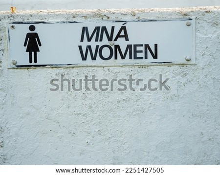 Sign women in Irish and English language on a changing room by a beach or toilet. Multi language culture concept. White wall with texture.