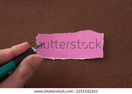 Hand writing something on pink torn paper.