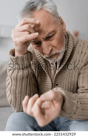 worried man with parkinsonian syndrome looking at trembling hand on blurred foreground Royalty-Free Stock Photo #2251432929