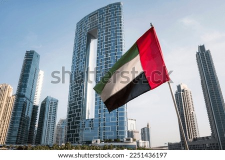 Unique view of UAE, United Arab Emirates national flag waving in the air with Dubai skyline in background. UAE National Day