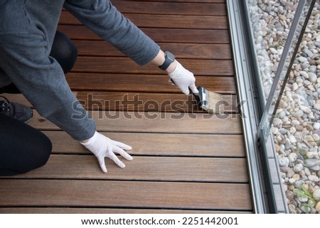 Worker refinishing wood, hand painting wooden deck floor with wood protection oil Royalty-Free Stock Photo #2251442001