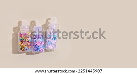 Close up Colorful glitters diffrent form for nail art and makeup in small jars beige background, copyspace. Minimal aesthetic photo with glitter for nails in glass bottles at sunlight, top view banner