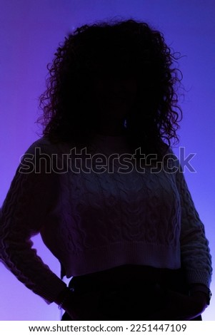 Silhouette of a middle-aged Caucasian woman with curly hair in front of a wall with blue led lights in a study room in Madrid.