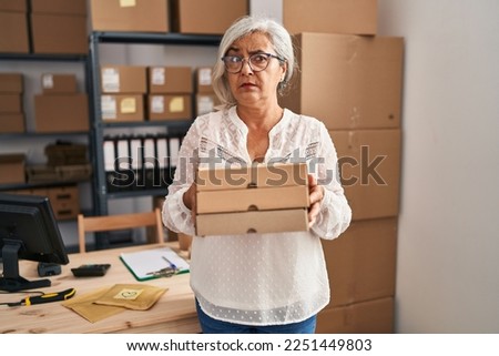 Middle age woman with grey hair working at small business ecommerce skeptic and nervous, frowning upset because of problem. negative person. 