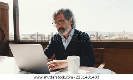 Middle-aged man working on laptop while with coffee sitting on balcony