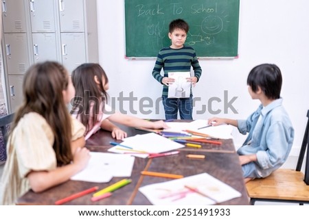 Children in class room happy laughing enjoy draw picture on paper and show to friend
