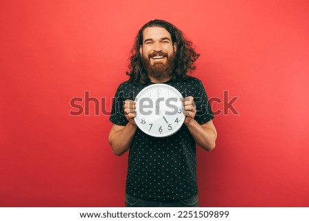 Young handsome man is holding a round white clock while smiling at the camera.