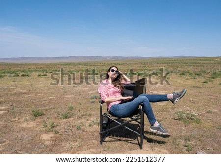 A young woman with a laptop is working against the background of a desert landscape. The concept of a freelancer, modern technology, work anywhere in the world