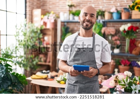 Young bald man florist smiling confident using touchpad at florist Royalty-Free Stock Photo #2251518281