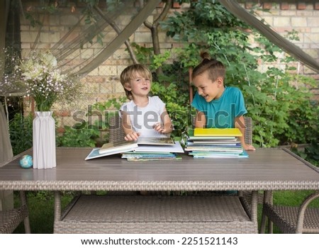 two preschool boys are sitting at table in garden, looking at, reading books. preparation for school, development of fantasy, childhood, communication with friend, with brother. Hello School