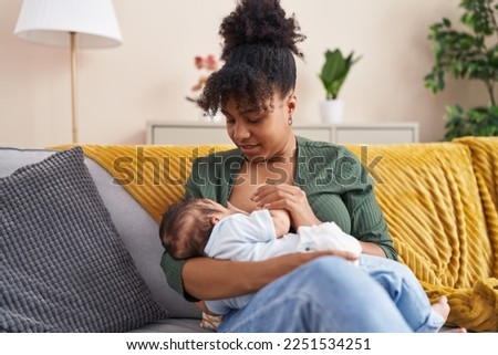 Mother and son sitting on sofa breastfeeding at home Royalty-Free Stock Photo #2251534251