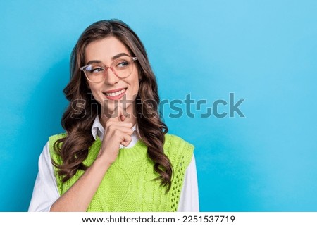 Photo portrait of attractive young woman eyewear touch chin look empty space wear trendy green outfit isolated on blue color background