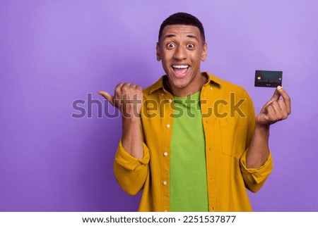 Photo of attractive young male impressed point empty space hold credit card dressed stylish yellow look isolated on violet color background