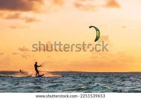 Sunset sky over the Indian Ocean bay with a two kiteboarders riding kiteboards with a green bright power kites. Active sport people and beauty in Nature concept image. Le Morne beach, Mauritius. Royalty-Free Stock Photo #2251539653
