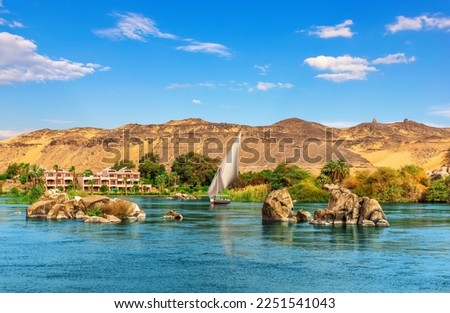 Nile stones and riverbank near Aswan and traditional sailboat, Upper Egypt Royalty-Free Stock Photo #2251541043