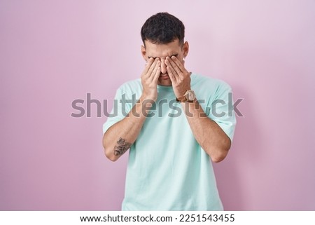 Handsome hispanic man standing over pink background rubbing eyes for fatigue and headache, sleepy and tired expression. vision problem 