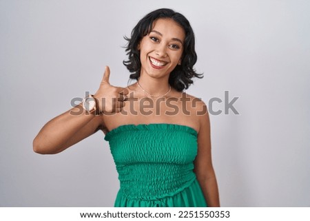Young hispanic woman standing over isolated background doing happy thumbs up gesture with hand. approving expression looking at the camera showing success. 