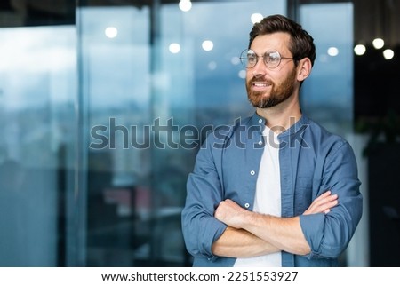 Portrait of a young successful man, businessman, freelancer, designer standing in the office, crossing his arms, confidently looking to the side Royalty-Free Stock Photo #2251553927