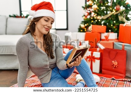 Young latin woman looking picture sitting by christmas tree at home