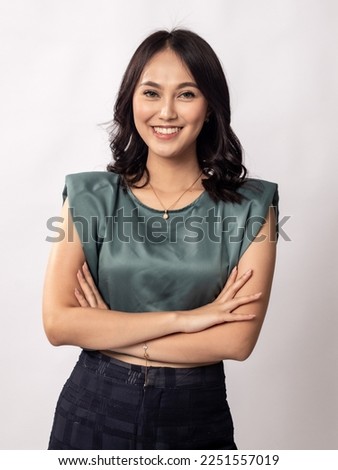 Portrait of a pretty Indonesian Asian girl in her 20s, wearing a light grey top and black trousers, smilingwith folded arms. Isolated on white background.