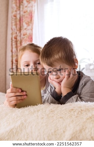 Children are lying on the bed, watching cartoons, playing a game on a smartphone