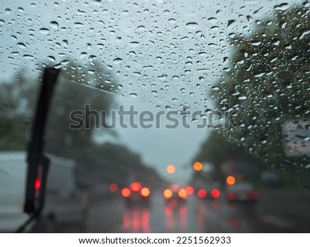 Closeup of rain drops on a windshield, blurry wipers cleaning the glass, road traffic with blurry car ligths. View from the driver's seat.