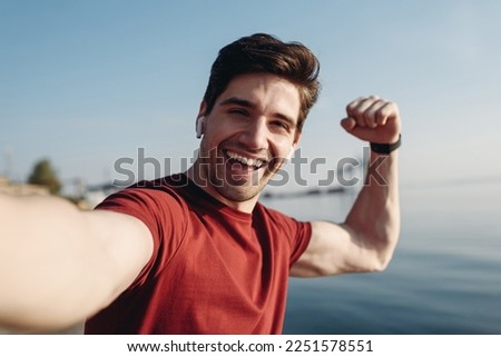 Close up young strong sporty sportsman man in sports clothes do selfie shot pov mobile cell phone do winner gesture warm up train at sunrise sun dawn over sea beach outdoor on pier seaside in morning