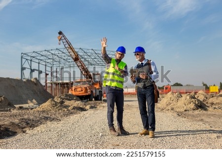 Two satisfied engineers talking at building site with construction structure in background
