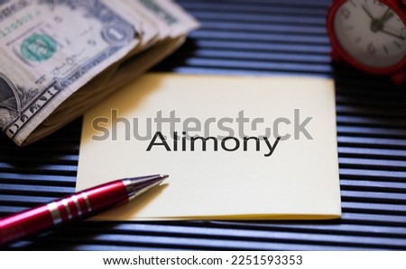 The word Alimony written on a piece of paper. A pen, an alarm clock and US dollar banknotes in the composition.
 Royalty-Free Stock Photo #2251593353
