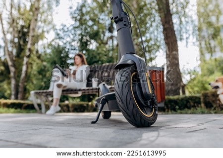 Pretty business woman in a white suit sits in a city park, drinks coffee and works on a digital tablet with an electric scooter in the foreground Royalty-Free Stock Photo #2251613995