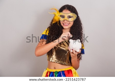 young teen girl, brazilian, with frevo clothes, carnival. with piggy bank and coin, closeup photo.
