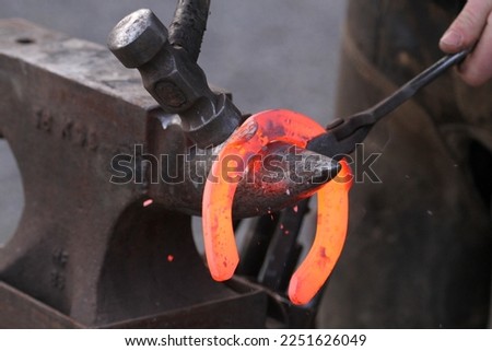 Red hot horseshoe being hammered and shaped on the anvil by the farrier. Equestrian Royalty-Free Stock Photo #2251626049