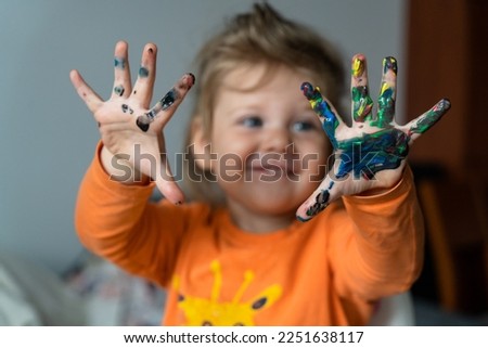 a happy little girl paints her hand with colored paints