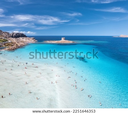 Aerial view of famous La Pelosa beach at sunny summer day. Stintino, Sardinia island, Italy. Top view of sandy beach, swimming people, clear blue sea, old tower and sky with clouds. Tropical seascape Royalty-Free Stock Photo #2251646353