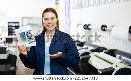 Portrait of positive woman printing office worker holding colour test page for printer and making presenting gesture. Royalty-Free Stock Photo #2251649013