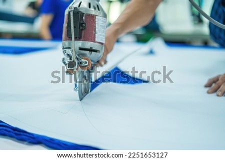 Man with cutter machine and personal protective equipment at garment industrial work place. Fabric cutter in Asian textile garment factory Royalty-Free Stock Photo #2251653127