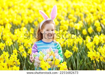 Easter egg hunt in spring garden. Kids searching for colorful eggs and sweets hidden in blooming flower field. Child with bunny ears and egg basket. Family Easter celebration. Girl in daffodil garden