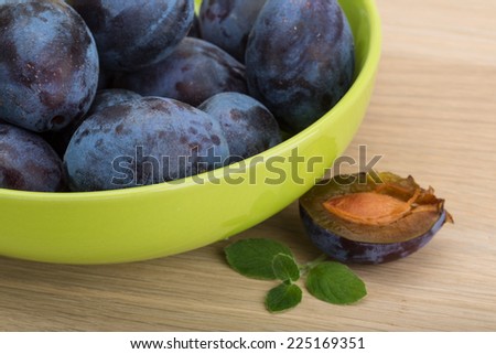 Fresh ripe prunes in the bowl on wooden background