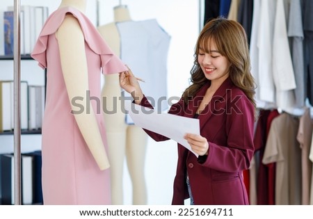 Millennial Asian young professional  female dressmaker designer seamstress with measuring tape briefing discussing working with dress on mannequin together in tailor workshop studio office.