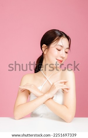 Young Asian woman gathered in ponytail with natural makeup on face have plump lips and clean fresh skin wearing white camisole on isolated pink background. Portrait of cute female model in studio.