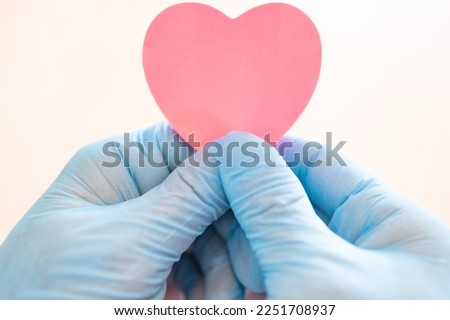 Male hands in blue medical gloves hold a pink heart symbol. Hands holding a pink heart.The gesture symbolizes of love. Help and volunteering, Insurance health care, pink love, Valentine day concept.