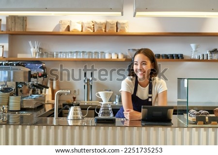 Smiling friendly asian girl barista, wearing apron, working at counter, brewing filter coffee, managing cafe shop. Royalty-Free Stock Photo #2251735253