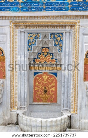 Outdoor ornate fountain inside the Topkapi palace complex in Istanbul.  Inlaid decorations over marble in golden, orange and blue patterns. Translation of Arabic text on the wall is "god is great" 