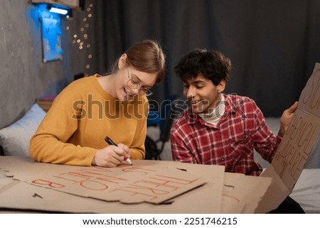 Teenage activists draw posters for a protest action for protecting the planet against global warming while sitting in a dorm room. Copy space