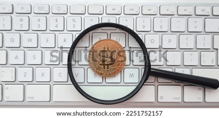 Bitcoin pending, magnifying glass and bitcoin coin on white computer keyboard. Cryptocurrency concept