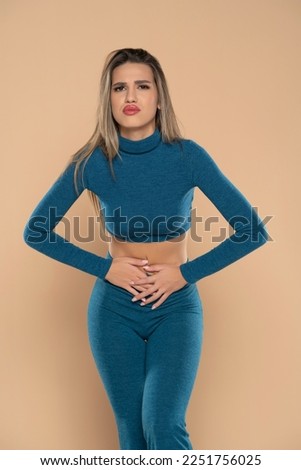 Close up woman holding belly, feeling discomfort, health problem concept, unhappy girl standing at beige studio background, suffering from stomachache, gastritis, abdominal pain, menst Royalty-Free Stock Photo #2251756025