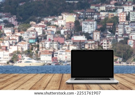 Laptop placed on a wooden table in front of the sea view. Blank black computer screen. Digital nomad or freelance work or remote working idea concept. online lecture or meeting. No people, nobody.