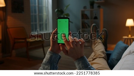 Close up shot of guy relaxing on couch at night, using smartphone with chroma key green screen and doing various gestures on display - technology, communications concept 