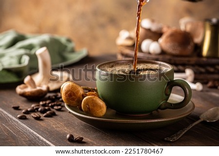 Trendy superfood mushroom coffee is pouring in green cup on wooden background. Healthy concept with copy space, selective focus. Royalty-Free Stock Photo #2251780467